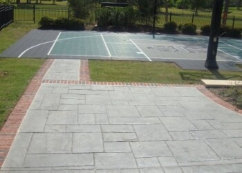 Stamped concrete basketball court in a park with a brick and concrete walkway. Stamped concrete basketball court with surrounding brick and concrete walkway in a park.