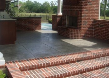 Finished stamped concrete patio with brick accents in a residential yard. Stamped concrete patio with brick steps and columns in a residential yard.