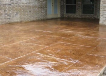 Finished stamped concrete patio in front of a brick house in Ephrata, Pennsylvania. Stamped concrete patio with a textured, brown finish in front of a brick house.