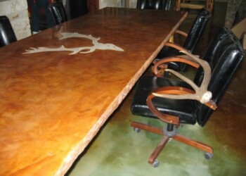 Large wooden conference table with a deer head inlay, surrounded by black leather chairs. Wooden conference table with a deer head inlay and black leather chairs around it.