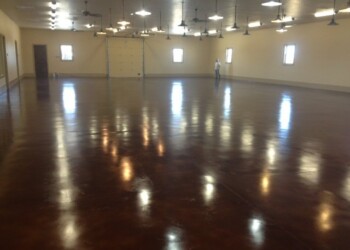Interior of a large commercial space with a polished concrete floor in ECD Concrete, located in the local area. Large indoor space with polished concrete floor and ceiling fans, person standing near the wall.