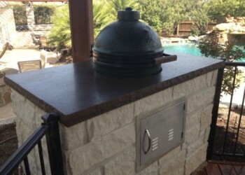 Stone outdoor pizza oven with dark dome in a backyard with pool and trees. Outdoor pizza oven with stone base and dark dome, in backyard setting.