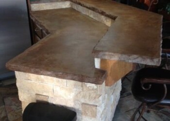Concrete kitchen island with stone base and wooden countertop in a home bar area. Concrete kitchen island with a stone base and wooden countertop in a home bar area.