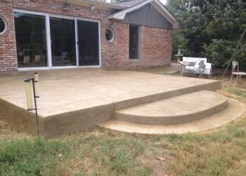 Finished stamped concrete patio with curved steps in a residential backyard. Concrete patio with stamped overlays and curved steps in a backyard.
