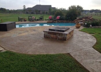 Stamped overlays on concrete patio with fire pit, pool, and outdoor seating in a rural backyard. Stamped concrete patio with fire pit and pool in a backyard setting.