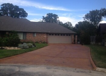 Concrete driveway stained with acid stain in front of a brick house in Euless, Texas. Concrete driveway with a reddish-brown stain in front of a brick house in a suburban neighborhood.