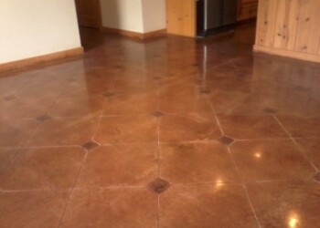 Polished concrete floor in a kitchen, showing a smooth, shiny surface with a reddish-brown color. Polished concrete floor with a reddish-brown finish in a residential kitchen area.