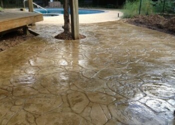 Finished stamped concrete patio with stone pattern in a backyard near a pool. Stamped concrete patio with a textured stone pattern in a backyard near a pool.