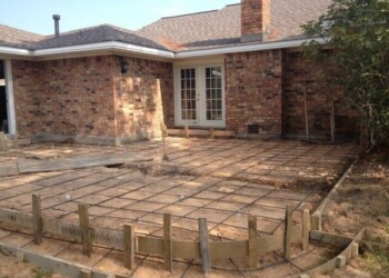 Concrete patio being poured and shaped in Euless, Texas, for a residential backyard. Concrete patio under construction in front of a brick house in Euless, Texas.