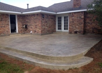 Finished stamped concrete patio with curved steps at a residential home in Euless, Texas. Stamped concrete patio with curved steps outside brick house in Euless, Texas.