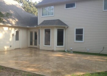 Finished stamped concrete patio outside a beige house in a residential area. Stamped concrete patio in front of a beige two-story house in a residential neighborhood.