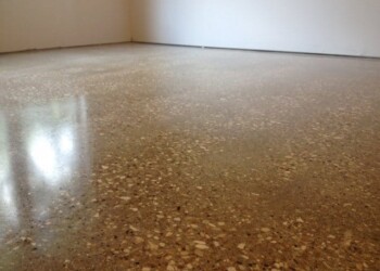 Finished polished concrete floor in a room, showing a smooth, reflective surface. Polished concrete floor in a room with white walls.