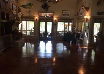 Polished concrete floor in a home interior with rustic decor and large windows. Interior of a home with polished concrete floor, decorated with mounted animal heads and framed pictures.