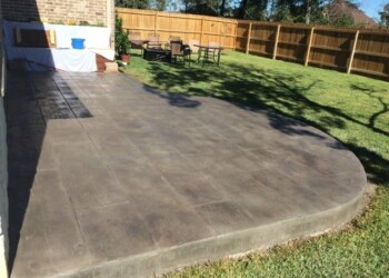 Finished stamped concrete patio in a backyard in Eads, Tennessee. Stamped concrete patio with curved edge in a backyard with lawn and outdoor furniture.