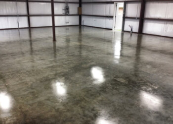 Sealed and waxed concrete floor in a warehouse, showing a smooth, reflective surface. Finished concrete floor with a sealed and waxed surface inside a warehouse.