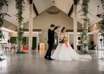 Bride and groom dancing at their wedding reception in a spacious, decorated hall. Bride and groom dancing in a decorated wedding hall with high ceilings and hanging chandeliers.