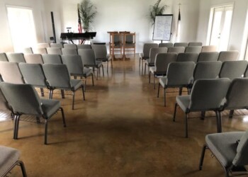 Room prepared for a presentation with acid stained concrete floor and seating arrangement. Interior of a room with acid stained concrete floor, chairs, and a small stage with a piano and whiteboard.