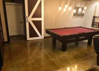 Game room with a red pool table, hanging lights, and a barn door in a residential basement. Interior of a game room with a red pool table and rustic decor.