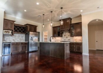 Kitchen with dark wood cabinets and polished concrete flooring in a home. Modern kitchen with dark wood cabinets, stainless steel appliances, and a polished concrete floor.