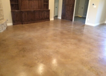 Finished acid-stained concrete floor in a living room, showing a smooth, glossy surface with warm earthy tones. Interior view of a finished acid-stained concrete floor in a living room.