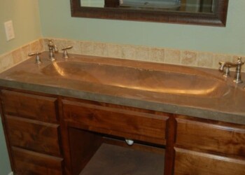 Copper bathroom sink installed on a wooden vanity in a bathroom. Copper bathroom sink with wooden vanity and beige tile backsplash.