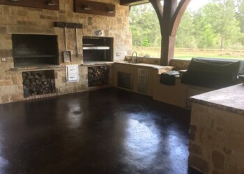 Finished outdoor patio with acid-stained concrete floor and stone fireplace in a rural area. Outdoor patio with stone fireplace and polished concrete floor in a rural setting.