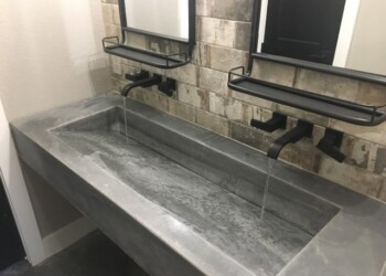 Concrete bathroom sink with two black faucets and wall-mounted mirrors. Concrete bathroom sink with two black faucets and wall-mounted mirrors in a modern setting.