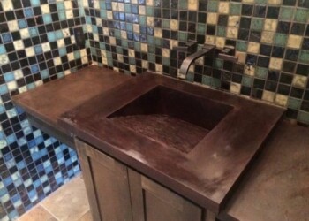 Concrete bathroom countertop with integrated sink and colorful tiled wall. Dark brown concrete countertop with integrated sink in a bathroom.