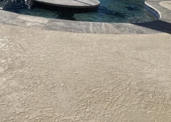 Textured concrete pool deck with a curved edge and a swimming pool in the background. Concrete pool deck with textured finish near a swimming pool.