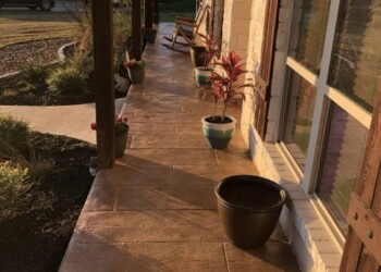 Residential porch in Euless, TX with stamped concrete, potted plants, and rocking chairs. Stamped concrete porch with potted plants and rocking chairs in a residential yard.