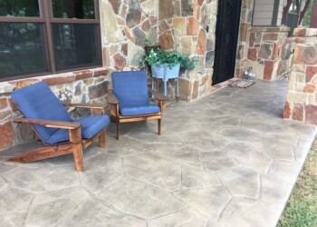 Stamped concrete patio with two blue chairs and stone house exterior in Eads, Tennessee. Stamped concrete patio with two blue cushioned chairs and a stone house exterior.