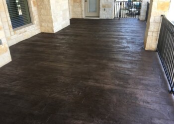 Finished stamped concrete porch with a wood-like appearance in a residential home. Stamped concrete patio with dark wood-like finish on a residential porch.