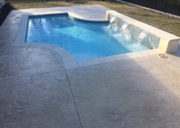 Stamped concrete overlays around the pool with water features in a backyard. Concrete pool deck with stamped overlays and water features in a backyard.