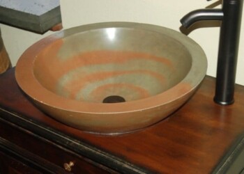 Copper sink installed on a wooden countertop with a black faucet. Copper sink with black faucet on wooden countertop in a kitchen.