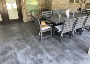 Stamped overlays on concrete patio with outdoor dining set in a backyard. Stamped concrete patio with outdoor dining table and chairs in a residential backyard.