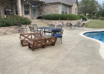 Stamped overlays on concrete patio with outdoor furniture and pool in a residential backyard. Concrete patio with stamped overlays and outdoor furniture near a house and pool.