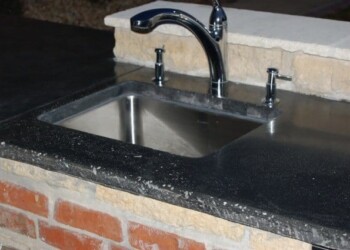 Kitchen sink installed on a black granite countertop with brick base in a residential setting. Stainless steel kitchen sink with black granite countertop and brick base.