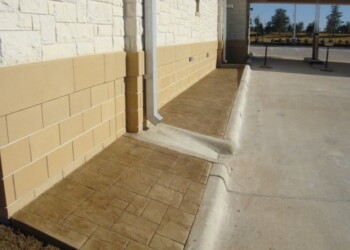 Concrete sidewalk and ramp at a commercial building in ECD, with brick wall and glass entrance. Concrete sidewalk and ramp with brick wall at a commercial building in ECD.