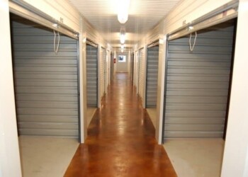 Storage units at ECD Concrete in a well-lit corridor with wooden flooring. Indoor storage units with metal roll-up doors in a corridor.