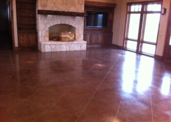Polished concrete floor in a living room with stone fireplace and large windows. Polished concrete floor in a living room with stone fireplace and wooden accents.