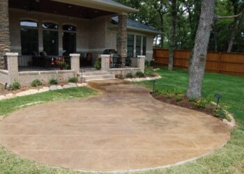 Stamped overlays on concrete patio at a residential home in Eads, Tennessee. Stamped concrete patio in front of a house with a porch and garden beds in Eads, Tennessee.