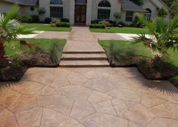 Stamped overlays on the concrete driveway enhance the home's curb appeal. Stamped concrete driveway with a stone pattern in front of a house.