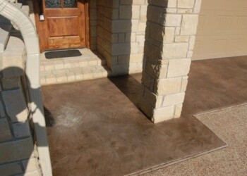 Stamped overlays on concrete porch at a home in Eads, Tennessee. Stamped concrete porch with brick columns and wooden door in a residential home.