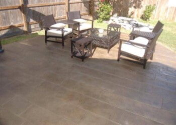 Stamped overlays on concrete patio with outdoor seating in a backyard. Stamped concrete patio with outdoor furniture in a backyard.