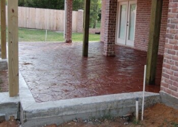 Finished stamped overlays on concrete patio at a home in Euless, Texas. Stamped concrete patio with brick house and wooden posts in a residential backyard.