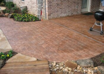 Stamped overlays on concrete patio in front of a brick house in Eads, Tennessee. Stamped concrete patio with a wood grain pattern in front of a brick house.